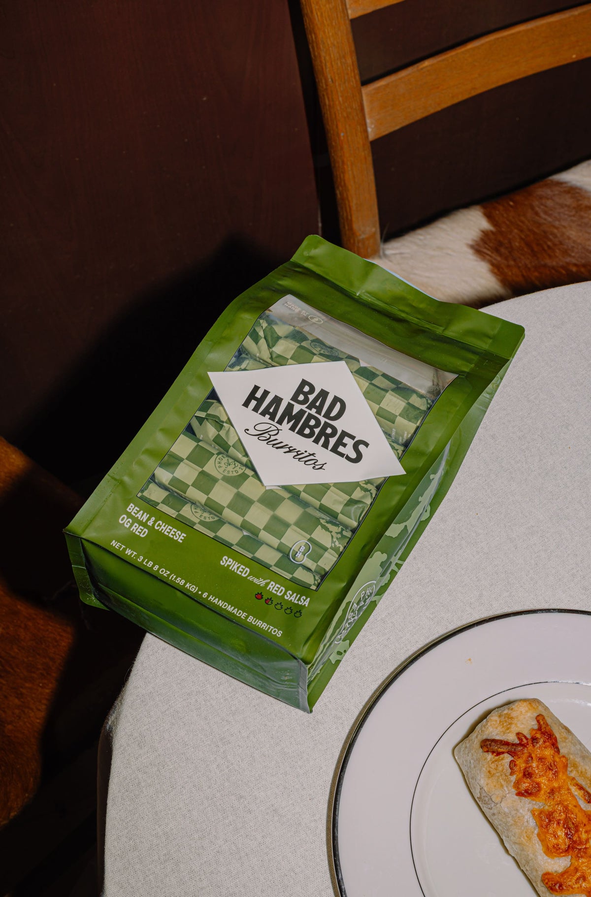 A 6 pack Bad Hambres OG Red package on top of a table, next to a burrito on a plate
